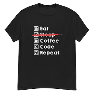 Puede incluir: Camiseta negra con un gráfico blanco. El gráfico enumera las palabras "Eat, Coffee, Code, Repeat", con la palabra "Sleep" tachada en rojo. La camiseta tiene cuello redondo y mangas cortas.