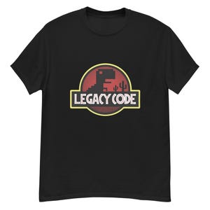 Puede incluir: Camiseta negra con un diseño gráfico de estilo retro. El diseño presenta un dinosaurio y un cactus pixelados dentro de un círculo rojo y amarillo. El texto "LEGACY CODE" se muestra en blanco. Una divertida camiseta gráfica.