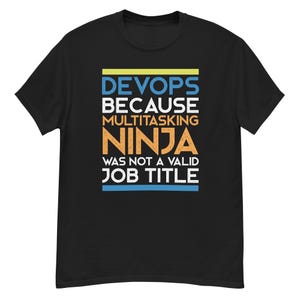 Könnte beinhalten: Schwarzes T-Shirt mit dem Text "DEVOPS BECAUSE MULTITASKING NINJA WAS NOT A VALID JOB TITLE" in Blau, Weiß, Orange und Gelb. Das Shirt hat einen Rundhalsausschnitt und kurze Ärmel.