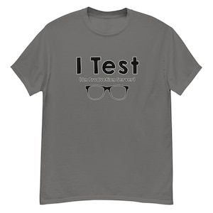 Peut inclure: Un t-shirt gris avec le texte noir "I Test", avec "(On Production Server)" en dessous. En dessous du texte se trouve une paire de lunettes noires. Le t-shirt est un vêtement décontracté.