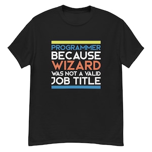 Puede incluir: Camiseta negra con el texto "PROGRAMMER BECAUSE WIZARD WAS NOT A VALID JOB TITLE" en blanco, naranja, azul y amarillo. La camiseta es de cuello redondo.