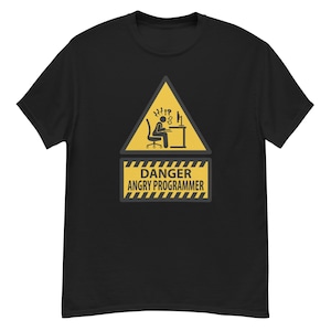 May include: Black t-shirt featuring a yellow warning sign with a stick figure at a desk, and the text "DANGER ANGRY PROGRAMMER". The sign is a humorous depiction of a programmer's workspace.