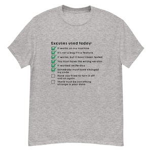 Puede incluir: Una camiseta gris jaspeada con el texto "Excuses used today:" y una lista de excusas comunes, como "It works on my machine" y "It's not a bug it's a feature." El texto es negro, con marcas de verificación verdes.