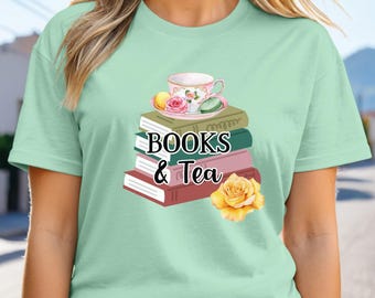 Puede incluir: Una camiseta de color verde menta claro con un gráfico de una pila de cuatro libros en tonos oliva, verde oscuro, rosa y granate. Sobre los libros hay una taza de té blanca con detalles florales, una rosa rosa y macarons. El texto dice BOOKS & Tea.
