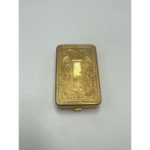 May include: A rectangular gold-toned metal compact case featuring an intricate embossed floral pattern across the lid and a smooth, plain rectangular center panel. The edges of the lid are framed with a textured border and a small latch is visible.