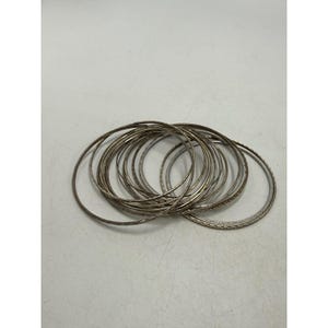May include: A set of multiple thin, circular silver-toned metal bangles. Each bangle features a delicate, repeating textured pattern along its outer surface. The bracelets are stacked together in an overlapping arrangement, showcasing their metallic finish and slender, lightweight construction.