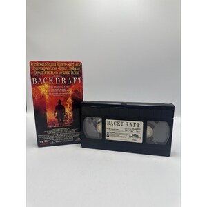 May include: A Backdraft VHS tape and its original cardboard sleeve. The sleeve features a fiery background with a silhouette of a firefighter and the movie title in white text. The black plastic tape has a white label with the title Backdraft.