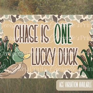 May include: A tan and green graphic with the text "CHASE IS ONE LUCKY DUCK". The design includes a cartoon duck wearing a hat, cattails, and a camouflage border. The words "AGE VARIATION AVAILABLE" are at the bottom.