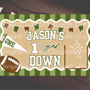 May include: A football-themed banner with the text "JASON'S 1st year DOWN." The design includes a football, a pennant that says "ONE," and a football field graphic. The background is a football.