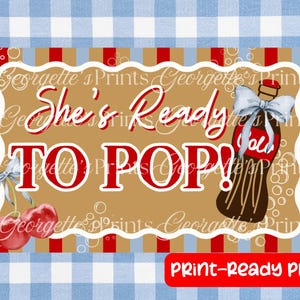 以下が含まれることがあります： 「She's Ready To Pop!」の赤い文字と、茶色のソーダボトルのイラストとサクランボが描かれたデジタルプリント。背景はベージュと赤のストライプ模様で、青と白のギンガムチェックのボーダーが付いています。