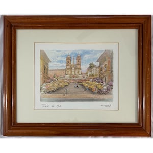 May include: Framed print of a European cityscape featuring a large church at the top of a staircase. The print has a cream-colored mat and a dark brown wooden frame. The print is signed by the artist.
