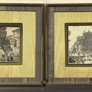 Op de afbeelding: Twee ingelijste architectuurprenten. Elke prent is een zwart-wit ets van een klassiek gebouw met figuren. De lijsten hebben een gouden binnenrand, een lichtgele stoffen passe-partout en een grijze buitenlijst.