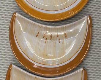 Op de afbeelding: Drie halvemaanvormige keramische schalen met een handgeschilderd oranje en crèmekleurig ontwerp. Elke schaal heeft een brede oranje rand, een witte binnenband en een crèmekleurig midden versierd met verticale penseelstreken en kleine oranje markeringen.