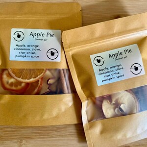 May include: Two brown paper pouches with clear windows, labeled "Apple Pie Summer pot." Each pouch contains dried apple slices, orange slices, cinnamon sticks, and star anise. The labels list the ingredients.