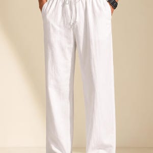 May include: White trousers featuring a relaxed, straight-leg fit with a comfortable elastic waistband and a matching white drawstring tie. The trousers are crafted from a lightweight, textured fabric and include side pockets for functional utility.