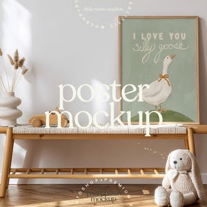May include: A wooden bench with a woven top holds a framed poster with a goose illustration and the text "I LOVE YOU silly goose." A vase with dried plants, a wooden car, and a stuffed bunny are also on the bench. The words "poster mockup" are in the foreground.