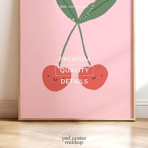 May include: A framed art print featuring a pair of smiling red cherries with green stems and leaves against a pink background. The print includes the text "PREMIUM QUALITY DETAILS".
