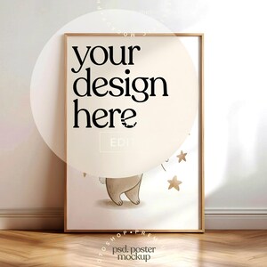 May include: A framed poster mockup with the text "your design here" in black. The poster features a light brown illustration of a bear and gold stars. The frame is a light brown color, and the background is a light beige.