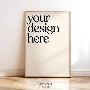 May include: A framed poster mockup with the text "your design here" in a bold, black font. The poster is set against a neutral wall and rests on a wooden floor, creating a clean and modern aesthetic.