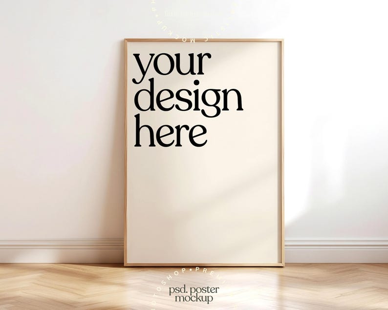 May include: A framed poster mockup with the text "your design here" in a bold, black font. The poster is set against a neutral wall and rests on a wooden floor, creating a clean and modern aesthetic.