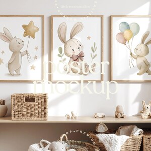 May include: Three framed nursery art prints with watercolour illustrations of bunnies holding balloons and a star. The prints are in light wood frames, displayed above a shelf with wicker baskets and toys. The text "poster mockup" is overlaid on the image.