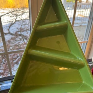 May include: A green, tree-shaped serving dish with three divided sections. The dish is made of ceramic or a similar material and has a glossy finish. The design is ideal for serving appetizers or snacks during the holidays.