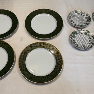 Könnte beinhalten: Ein Set aus sechs weißen Keramikplatten mit dekorativen grünen und goldenen Rändern. Die größeren Teller haben durchgehend grüne oder gemusterte Ränder, während die kleineren Teller ein gewebtes Design mit floralen Akzenten aufweisen.