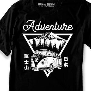 Puede incluir: Camiseta negra con un gr&aacute;fico blanco de una camioneta Volkswagen vintage conduciendo por un paisaje de monta&ntilde;a. El texto "Adventure" est&aacute; por encima de la camioneta y el texto "富士山 日本" est&aacute; por debajo de la camioneta.