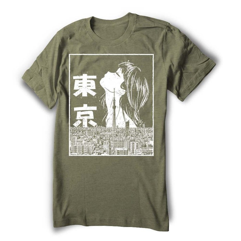 Puede incluir: Una camiseta verde con un estampado gr&aacute;fico blanco de una mujer mirando hacia arriba a un paisaje urbano con la palabra japonesa "Tokio" escrita verticalmente en blanco.