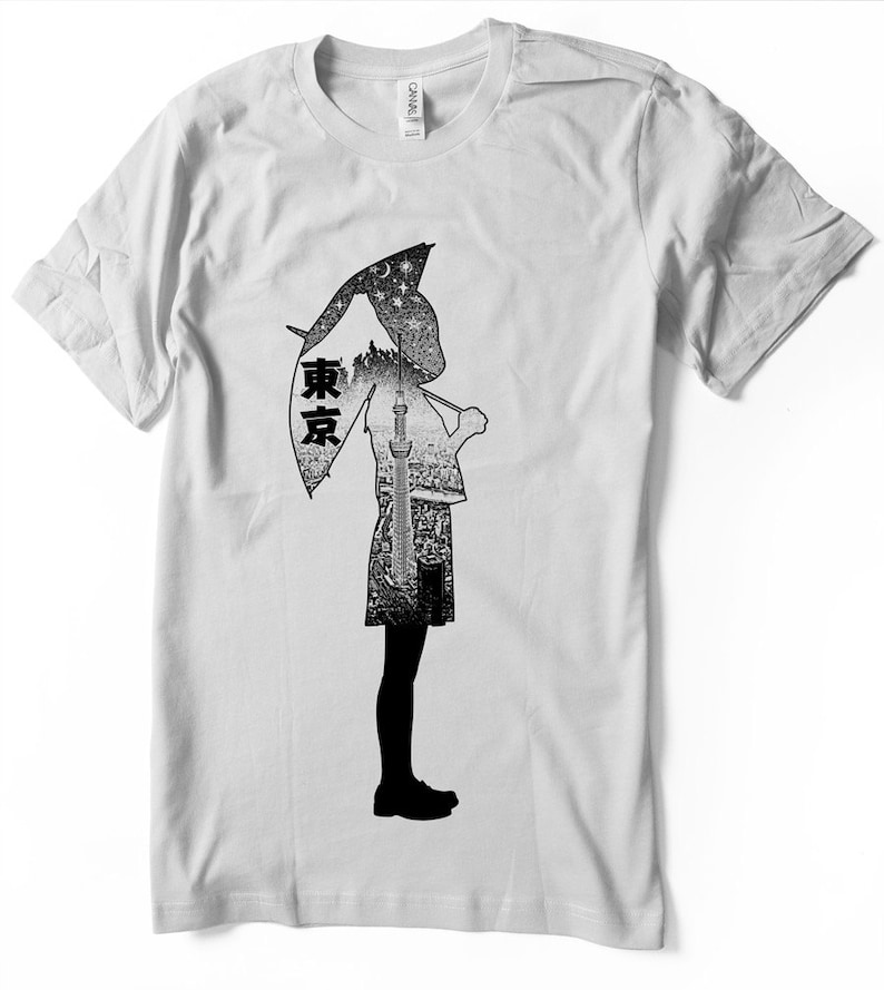 May include: A white t-shirt with a black and white graphic print of a person holding an umbrella. The umbrella is shaped like a city skyline with the word "東京" (Tokyo) written on it.