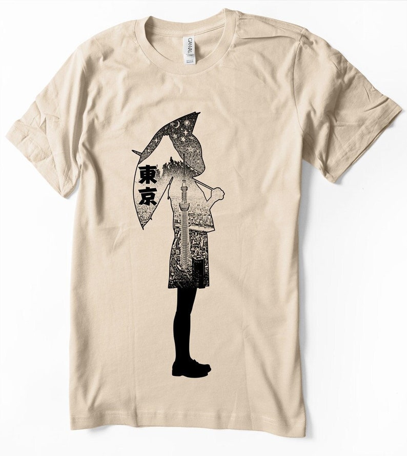 May include: A beige t-shirt with a black silhouette of a person holding an umbrella. The umbrella is made up of a cityscape with the word "東京" (Tokyo) written on it.
