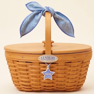 May include: A woven wooden basket with a light brown finish, featuring a wooden lid and a central handle tied with a light blue fabric ribbon. A silver oval plaque reads Century, and a blue star-shaped tag displays the year 2000 in white text.