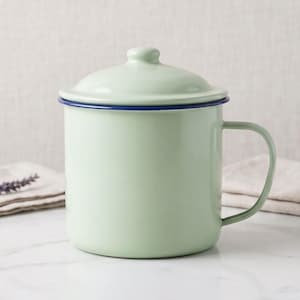 May include: A light sage green enamel mug with a matching lid and a dark blue rim. The cylindrical container features a smooth, glossy finish and a single side handle, presenting a clean, functional design for holding liquids or small items.
