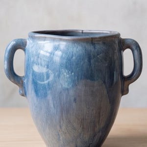 May include: A ceramic vessel featuring a rounded body and two symmetrical side handles. The exterior is finished with a glossy, variegated blue glaze that transitions between deep navy and lighter sky blue tones with visible brushstroke textures.