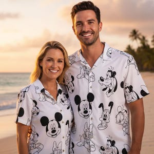Może przedstawiać: Białe koszule zapinane na guziki z czarno-białym nadrukiem postaci z kreskówek. Koszule przedstawiają Myszkę Miki, Minnie, Goofy'ego i Kaczora Donalda. Para uśmiecha się na plaży.
