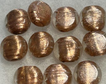May include: A collection of ten round glass beads, each featuring a clear outer layer and a core of shimmering, metallic copper-colored glitter. The beads have a smooth, polished surface with subtle horizontal striations visible within the glass.