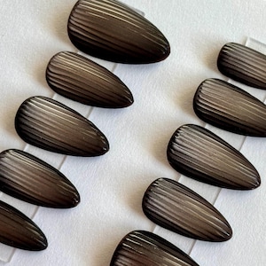 May include: A collection of teardrop-shaped, dark brown nail art pieces. Each piece has a ridged texture, creating a striped pattern. The pieces are arranged on a white surface, showcasing their glossy finish and unique design. Ideal for nail art enthusiasts.
