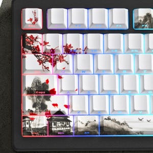 May include: A mechanical keyboard with white keycaps featuring artistic designs of red flowers and mountain landscapes. The keyboard has a black frame and a colourful LED backlight.