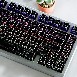 May include: A silver mechanical keyboard with black keycaps and white lettering. The keys are backlit with various colors, including red, blue, and green. The keyboard has a standard layout with function keys and a number pad.