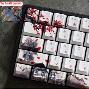May include: A close-up of a mechanical keyboard with custom keycaps. The keycaps feature Japanese-inspired art, including cherry blossoms and landscape paintings. The keyboard has a black frame and white keycaps with Japanese characters.