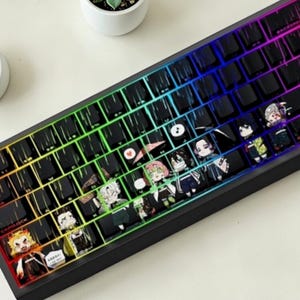 Op de afbeelding: Een zwart mechanisch toetsenbord met keycaps met anime-personageontwerpen. Het toetsenbord heeft een regenboog LED-achtergrondverlichting, waarbij de kleuren over de toetsen overgaan. De keycaps hebben kleurrijke illustraties van anime-personages.