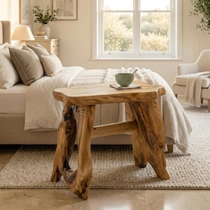 May include: A natural wood side table featuring a thick, live-edge tabletop supported by two sturdy, organic-shaped tree trunk legs. The light brown wood displays a prominent grain pattern and textured, uneven edges, providing a stable base for the table.