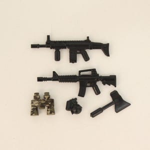 May include: A collection of black toy weapons, including two rifles, a grenade, a hatchet, and binoculars with a camouflage pattern. The items are arranged on a white surface.