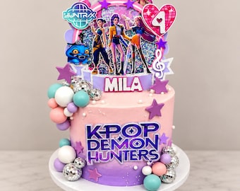 May include: A multi-tiered cake topper featuring K-Pop Demon Hunters characters, a glittery background, and a heart with the number 4. The base includes the text MILA and K-POP DEMON HUNTERS, decorated with purple stars, disco balls, and pastel spheres.