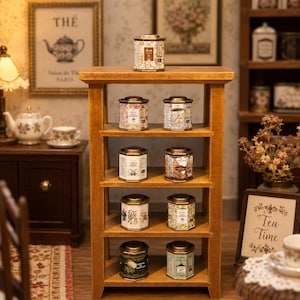 Op de afbeelding: Een houten plank toont verschillende kleine, decoratieve theeblikjes met diverse labels. De blikjes zijn op de planken gerangschikt en tonen hun unieke ontwerpen en kleuren. De achtergrond omvat een ingelijste foto en een bord met "Tea Time".