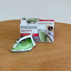 以下が含まれることがあります： 緑と白のデザインの、Black+Decker Easy Steamコンパクトアイロンのミニチュア。アイロンは、アイロンと「2X Smoother Glide」の文字も表示されている製品ボックスの隣にあります。