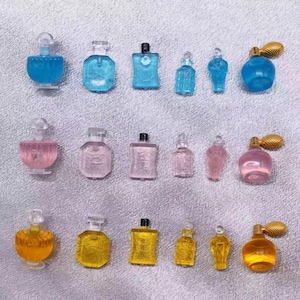 May include: Collection of miniature perfume bottles in various shapes and colors, including blue, pink, and yellow. Some bottles have gold-colored sprayers, while others have clear stoppers. The bottles are arranged on a light gray surface.