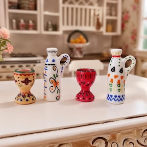 May include: A set of four miniature ceramic kitchen items including two egg cups and two handled oil cruets. The items feature hand-painted colorful patterns in yellow, red, blue, green, and orange, with intricate floral and geometric motifs.