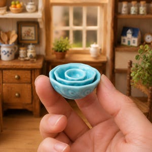 Pode incluir: Um conjunto de três taças de cerâmica em miniatura encaixadas com um esmalte azul claro. As taças apresentam um design liso e arredondado com um acabamento brilhante, empilhadas umas dentro das outras para mostrar os seus tamanhos variados.