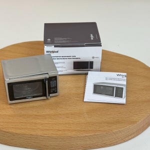 以下が含まれることがあります： ミニチュアのシルバーのWhirlpoolカウンター電子レンジ。ドアが開いており、コントロールパネル、箱、マニュアルがあります。箱とマニュアルには、Whirlpoolのロゴと製品情報が記載されています。